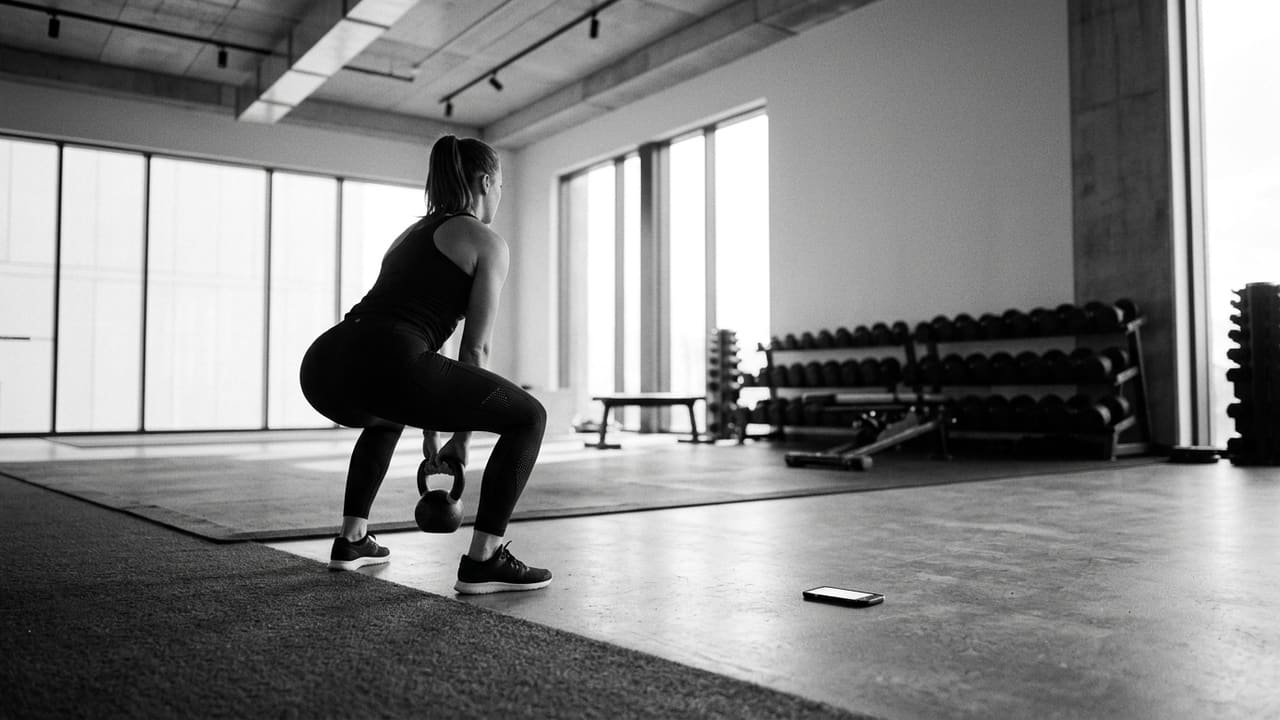 An athlete performing a kettlebell goblet squat in a brightly lit, minimalist gym
