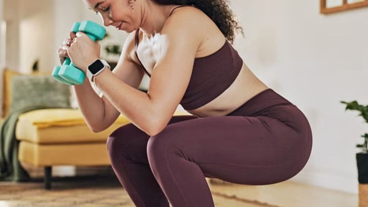 Woman doing a dumbbell squat at home, following a saved workout video